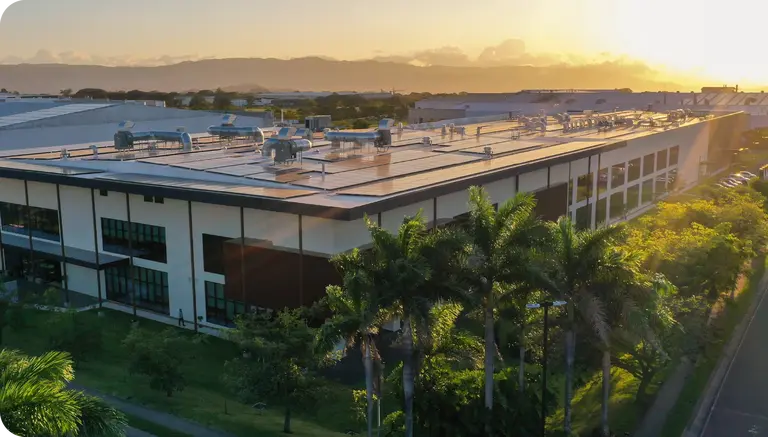 Aerial view of the Motiva Implants Sulayom manufacturing facility in Costa Rica, featuring solar panel roofing and surrounded by lush greenery at sunset.